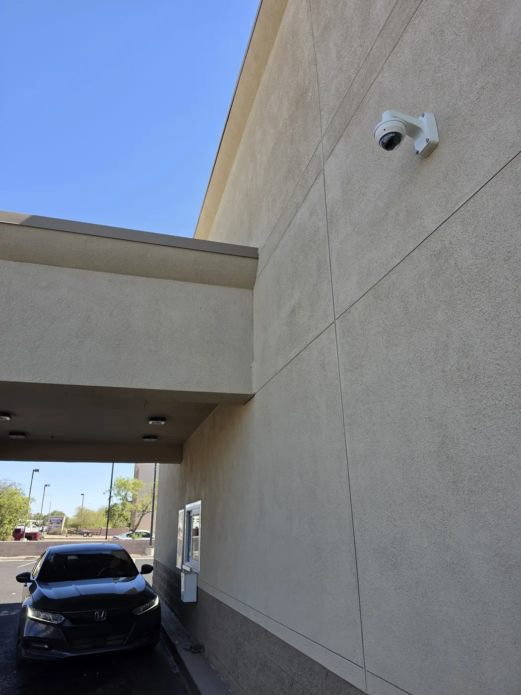 Exterior security camera installed beneath a commercial building overhang near parking